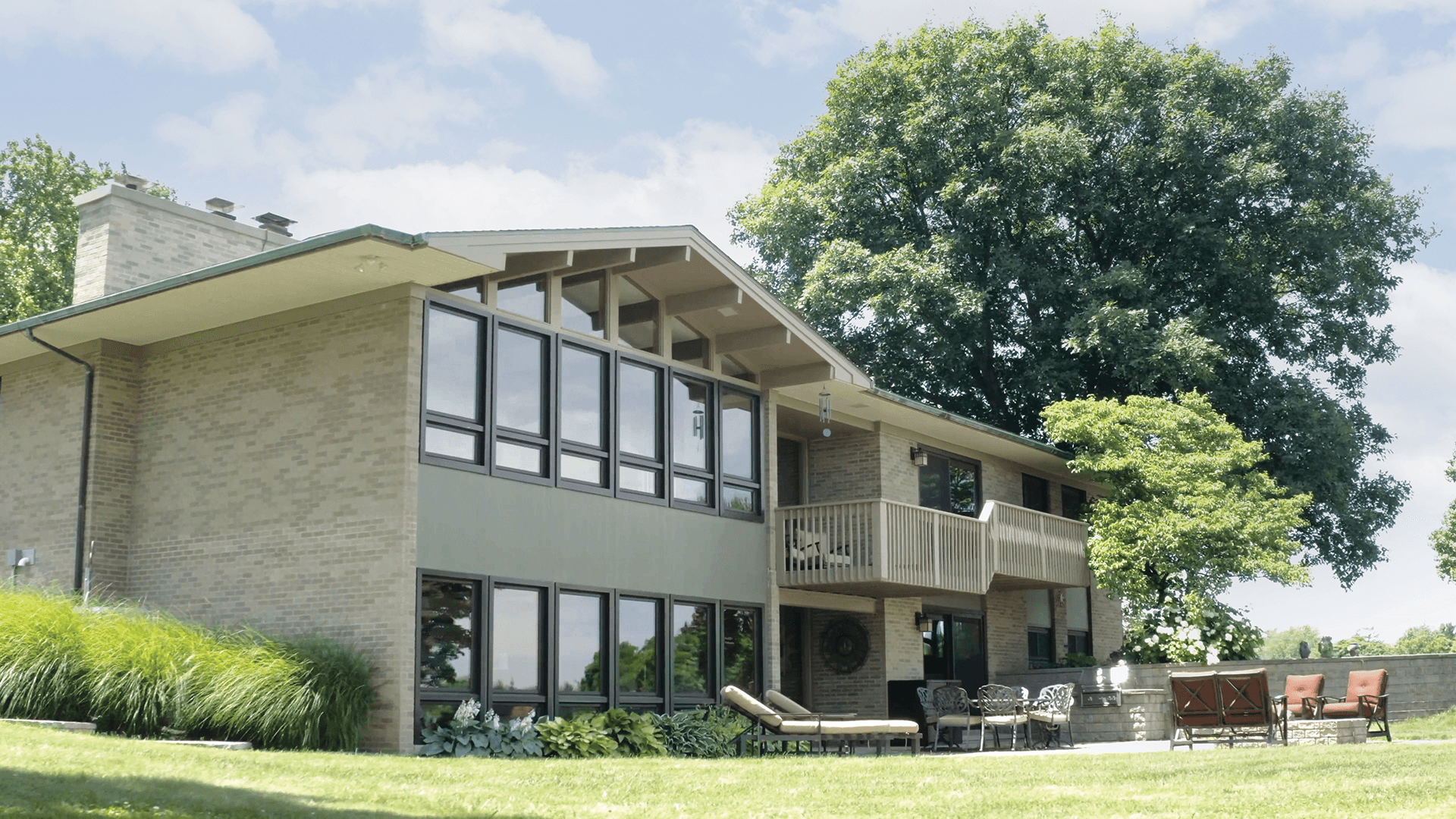Exterior backyard view of a brick and green home with a wall of windows featuring picture, special shape, and awning windows.