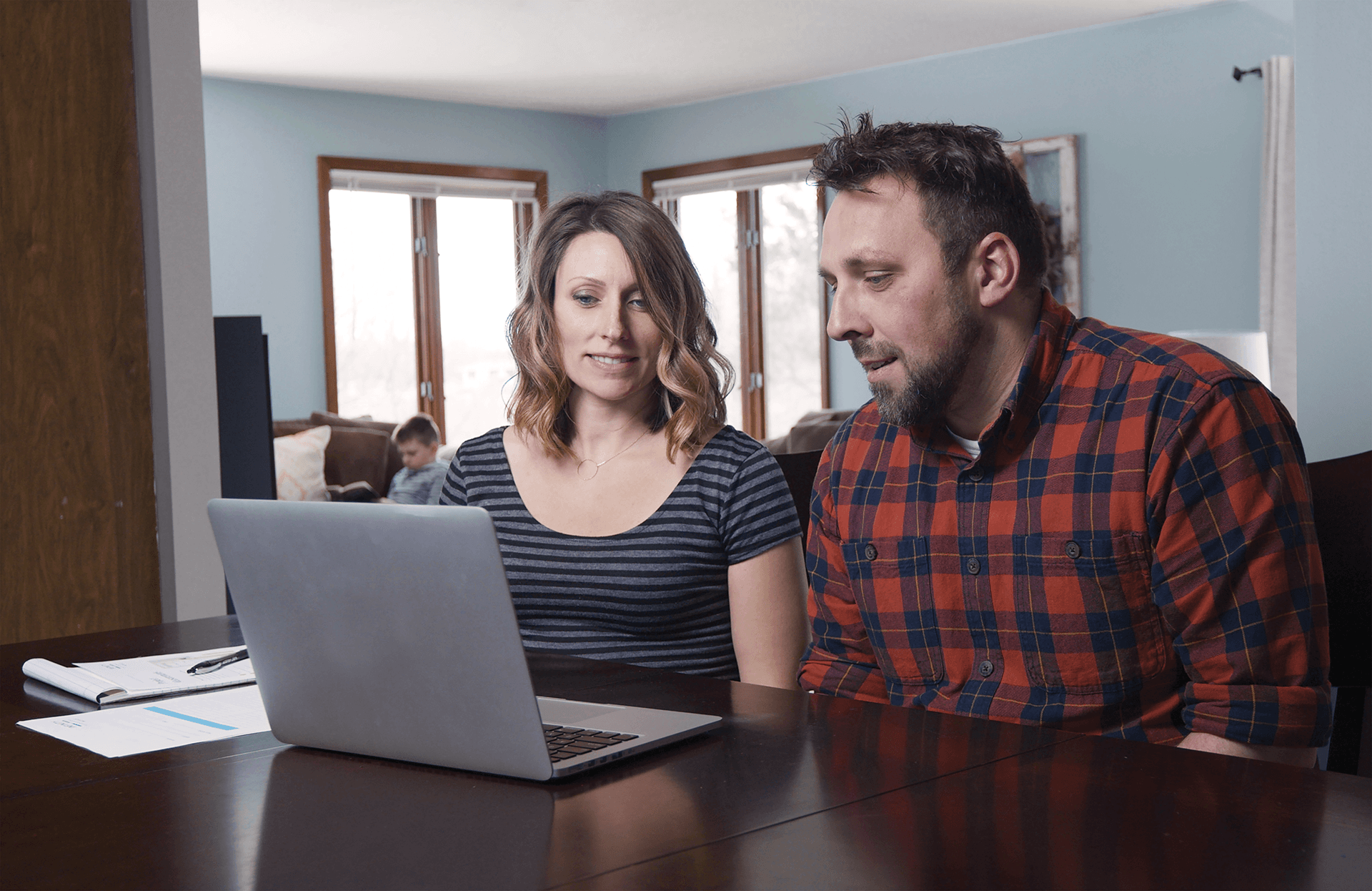 A middle-aged couple sit in front of a laptop computer during a virtual design consultation for replacement windows.