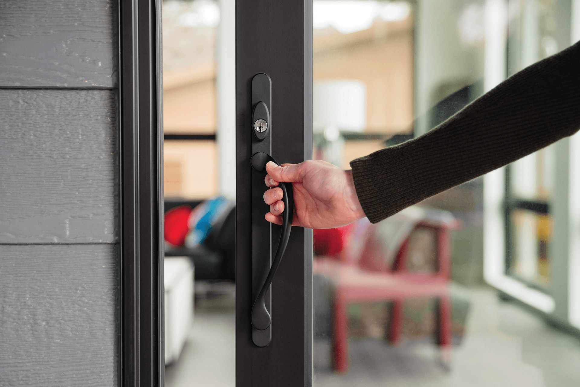 A woman holds onto a black patio door handle as she opens the door from the outside.