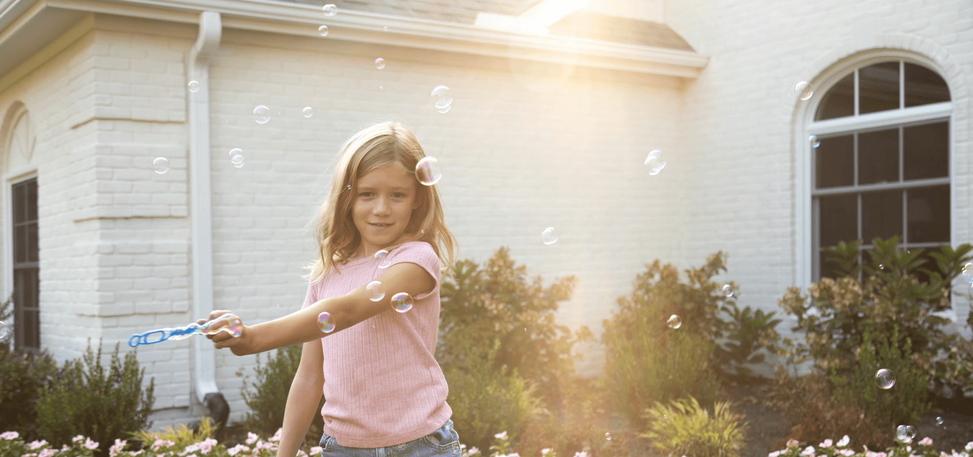 A young girl playing with bubbles outside of a home with Infinity from Marvin windows.